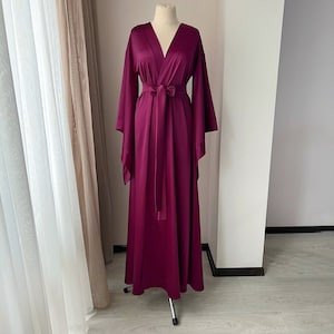 May include: A long, burgundy satin robe with a V-neck and wide sleeves. The robe has a matching sash that ties at the waist.