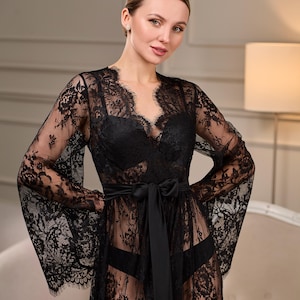 Elegant black lace robe with a dramatic train, sheer floral embroidery, and flowing bell sleeves. A satin belt cinches the waist, creating a refined silhouette.