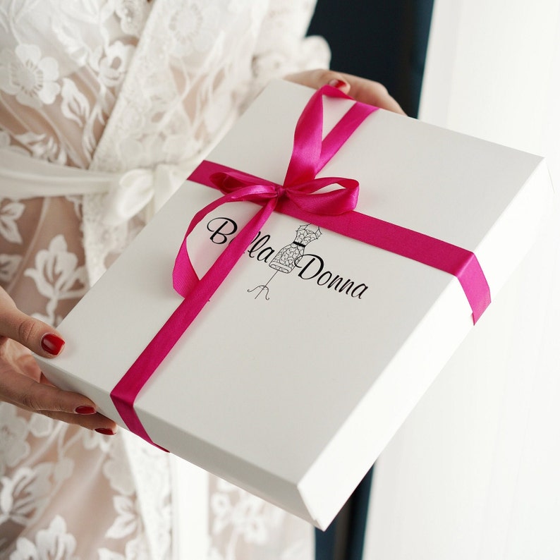 May include: White gift box with a pink ribbon and the text "Bella Donna" in black lettering. The box is decorated with a small black and white illustration of a dress form.