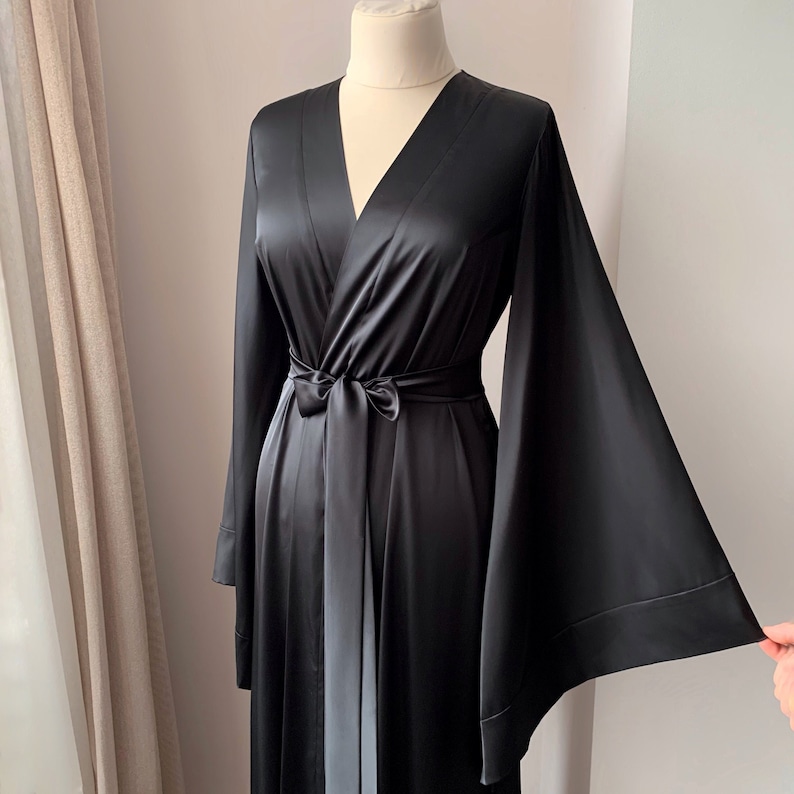 Puede incluir: Bata de sat&eacute;n negro con mangas anchas y cintur&oacute;n a juego. La bata se exhibe en un maniqu&iacute; y tiene un dise&ntilde;o de cuello en V. La tela tiene un ligero brillo y el aspecto general es elegante y fluido.