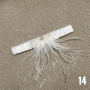 May include: White satin garter with a white feather trim and a pearl accent. The garter has a delicate lace flower design.