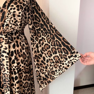 May include: A long-sleeved, brown and black leopard print dress with a wrap style bodice and a tie belt. The dress has wide, flowing sleeves.