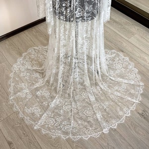 May include: A white lace wedding dress with a long train. The dress features intricate floral patterns and a scalloped edge. The fabric appears delicate and sheer, with a flowing design.