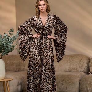 Puede incluir: Una bata larga de estampado de leopardo marr&oacute;n y negro con cuello en V y mangas largas. La bata tiene un lazo en la cintura y una abertura en la parte delantera.