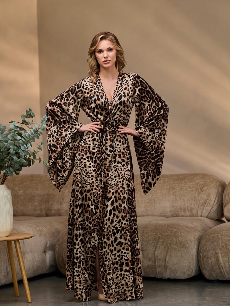Puede incluir: Una bata larga de estampado de leopardo marr&oacute;n y negro con cuello en V y mangas largas. La bata tiene un lazo en la cintura y una abertura en la parte delantera.
