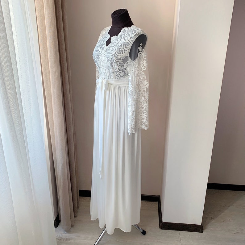 May include: A white lace robe with long sleeves and a V-neckline. The robe has a sash tie at the waist and is made of a soft, flowing fabric.