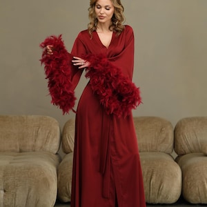 May include: A long, red satin robe with feather trim on the sleeves. The robe has a sash tie and a front slit.