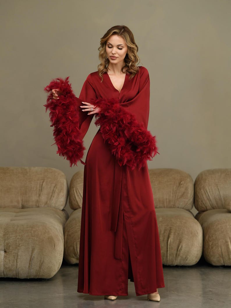 May include: A long, red satin robe with feather trim on the sleeves. The robe has a sash tie and a front slit.