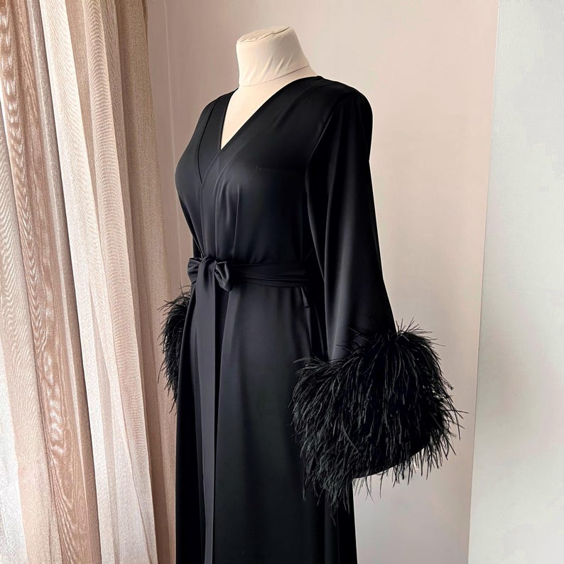 May include: A black satin robe with long sleeves and a V-neck. The sleeves have black feather trim.