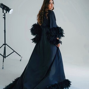 May include: A long black satin robe with feather trim around the cuffs, hem, and neckline. The robe is worn by a person with long brown hair.