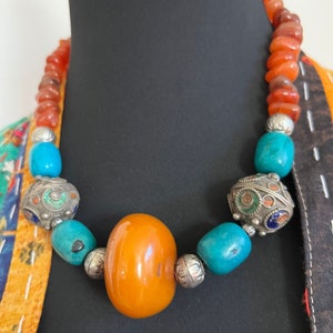 May include: A necklace made of orange carnelian, turquoise, and silver beads. The necklace features a large amber bead in the centre.