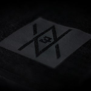 May include: A black patch with a stylized logo featuring a geometric design with intersecting lines and a central letter "Z".