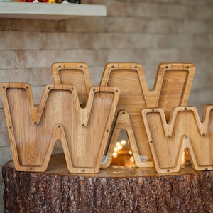 Three wooden letters on a tree stump, each with a small hole in the center.