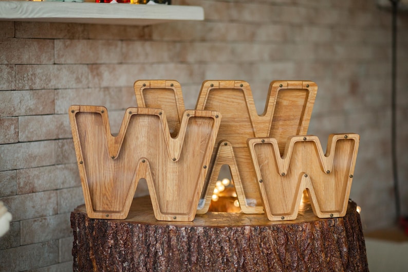 Three wooden letters on a tree stump, each with a small hole in the center.