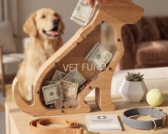 May include: A dog-shaped wooden piggy bank with a clear acrylic front panel, featuring the text VET FUND printed on the glass. The bank contains US dollar bills and coins. Nearby are a tan leather leash, a notebook labeled VETERINARY RECORDS, and a gray collar.