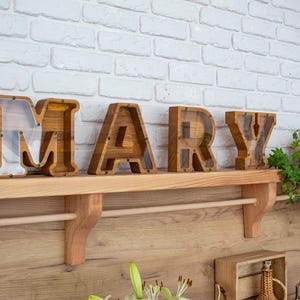 A wooden shelf displaying wooden letters spelling out the name 'MARY' in a room with a white brick wall.