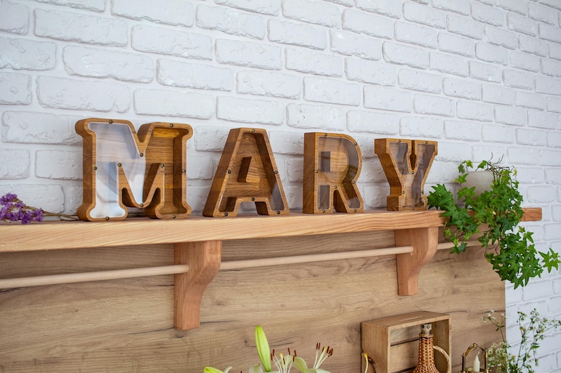 A wooden shelf displaying wooden letters spelling out the name 'MARY' in a room with a white brick wall.