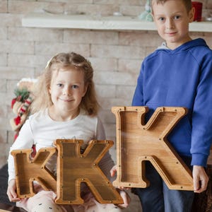 A young girl and boy are holding wooden letters, K and K, in front of a brick wall.