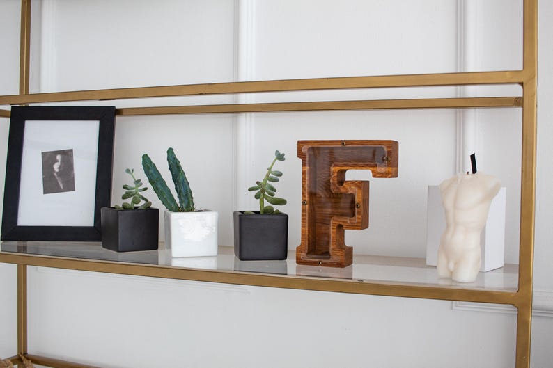 a shelf with various decorative items, including a black and white photo frame, two potted succulents, a wooden letter 'F', and a white candle.