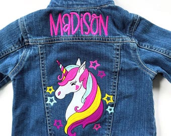 May include: A blue denim jacket with a pink unicorn and stars embroidered on the back. The name "MADISON" is embroidered in pink on the back of the collar.