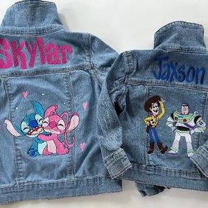 May include: Two denim jackets with embroidered designs. One jacket has a pink and blue Stitch and Angel character design with the name "Skylar" embroidered on the back. The other jacket has a blue embroidered design of Woody and Buzz Lightyear from Toy Story with the name "Jaxson" embroidered on the back.
