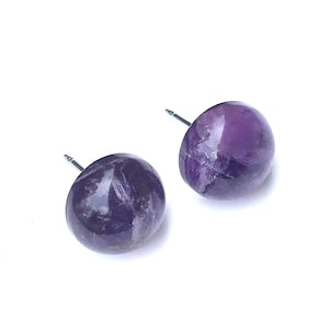 May include: A pair of amethyst stud earrings with silver posts. The amethyst stones are a deep purple color and have a natural, irregular shape.