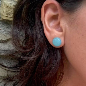 May include: A pair of light blue round stud earrings. The earrings are made of a smooth, polished material.