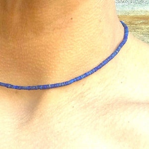 May include: A delicate necklace composed of small, dark blue beads. The necklace is worn around the neck, showcasing its simple yet elegant design. The beads appear to be evenly sized and spaced, creating a uniform appearance.