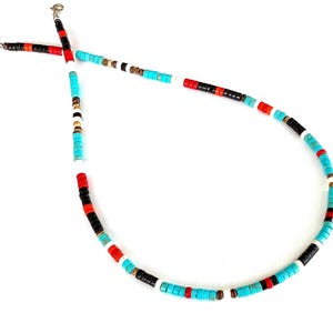 May include: A vibrant beaded necklace featuring turquoise, red, black, white, and brown beads. The necklace is strung on a silver chain. The beads are small and cylindrical, set against a white backdrop.