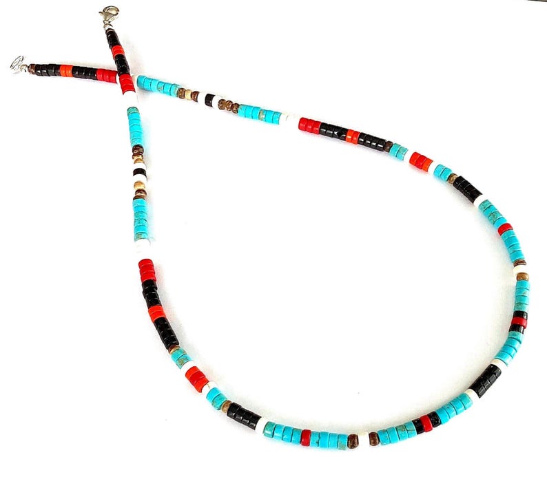 May include: A vibrant beaded necklace featuring turquoise, red, black, white, and brown beads. The necklace is strung on a silver chain. The beads are small and cylindrical, set against a white backdrop.