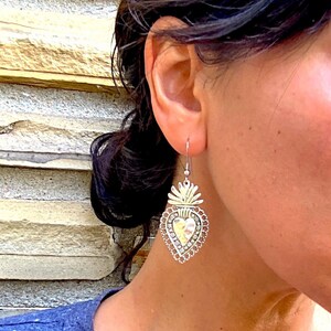 May include: Silver heart-shaped earrings with a detailed design and a textured finish. The earrings feature a raised heart with a flame-like design at the top.