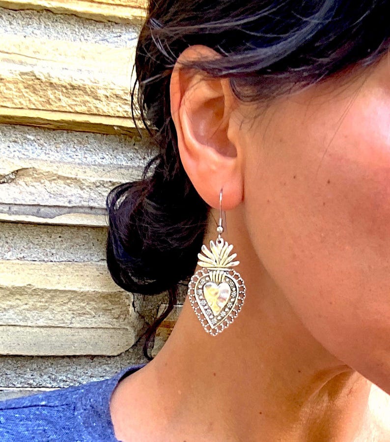 May include: Silver heart-shaped earrings with a detailed design and a textured finish. The earrings feature a raised heart with a flame-like design at the top.