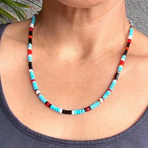 May include: A multi-coloured beaded necklace with turquoise, red, black, white, and orange beads. The necklace is made of small, round beads strung together, creating a vibrant accessory. The necklace is worn around the neck.