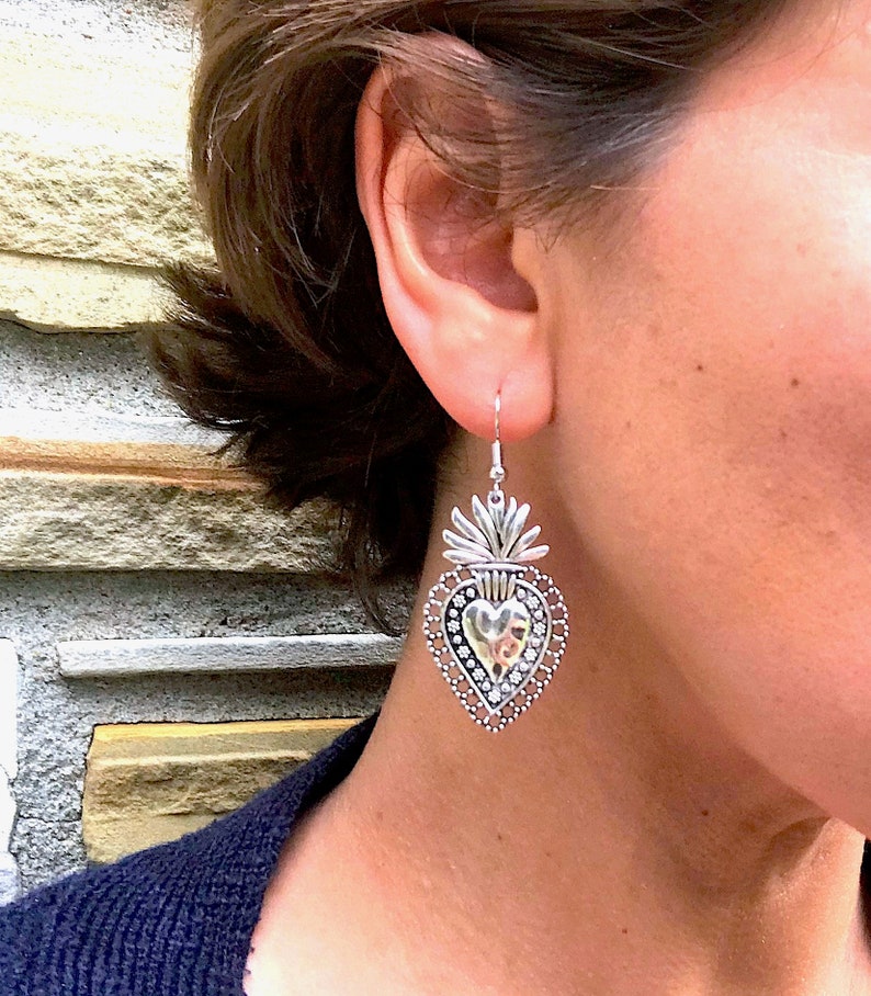 Silver dangle earrings featuring the textured design of the sacred heart. Measures approximately 5 cm in length.