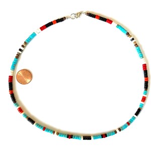 May include: A necklace made of small, flat beads in turquoise, red, black, white, and gold colours. The beads are strung together. The clasp is silver. A penny is next to the necklace for size comparison.