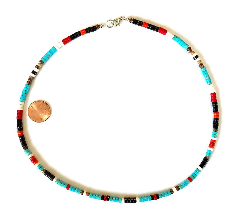 May include: A necklace made of small, flat beads in turquoise, red, black, white, and gold colours. The beads are strung together. The clasp is silver. A penny is next to the necklace for size comparison.