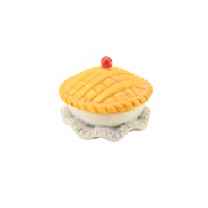 May include: A miniature pie with a lattice crust, topped with a red cherry. The pie sits on a decorative, scalloped-edge plate. The crust is golden brown, and the filling is a creamy white color.