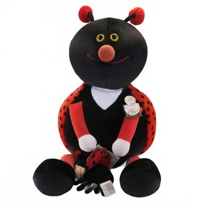 May include: A plush ladybug toy with a large black head, yellow eyes, and a red nose. The body is black with red wings featuring black spots. It has red arms with white hands, black feet, and two antennae with red tips. A small ladybug is attached.