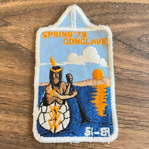 May include: Embroidered patch with a light blue sky background and a Native American figure paddling a canoe on blue water. The patch has the text "SPRING '74 CONCLAVE" in orange, with a setting sun and a white cloud. The bottom right corner has the text "51-83".