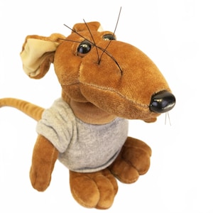 May include: A brown plush mouse toy featuring a soft, light gray t-shirt, large ears, a black plastic nose, and long, thin black whiskers. The stuffed animal has a smooth, velvet-like texture and a long tail extending from the back of its body.
