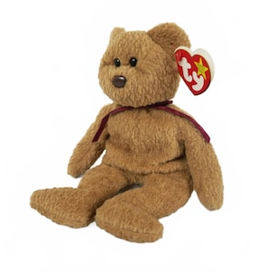 May include: A brown plush teddy bear with a burgundy ribbon around its neck and a red heart-shaped tag. The bear has black eyes and a brown nose. The tag has the word "ty" on it.