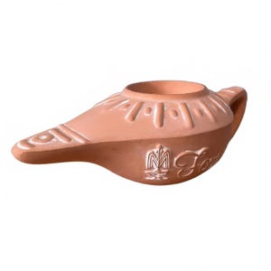 May include: A terracotta oil lamp with a rounded body, a tapered spout, and a handle. The top surface features embossed radial lines and a central circular opening. A small emblem and the partial script text Font are molded into the side.