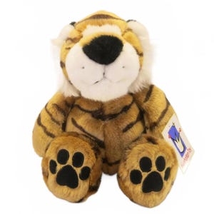 May include: A plush tiger toy with orange and black stripes, a white muzzle, and a black nose. The stuffed animal features black paw pads on its feet and a white tag attached to its side with the text Manhattan Toy printed in blue and red.