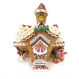 May include: A gingerbread house figurine featuring a clock tower, white icing roof details, and candy decorations. A snowman wearing a purple hat and a gingerbread person in a red outfit stand at the entrance, which has candy cane pillars.