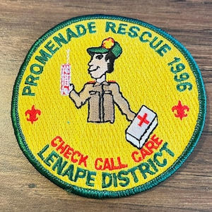 May include: Embroidered patch with a yellow background and green border. The patch features a cartoon figure holding a walkie-talkie and a first aid kit. Text includes "Promenade Rescue 1996" and "Check Call Care Lenape District".