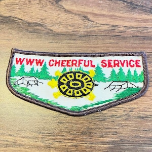 May include: Embroidered patch with the text "WWW CHEERFUL SERVICE" in red. The patch features a yellow and black turtle design, green trees, and two white tents. The patch has a brown border.