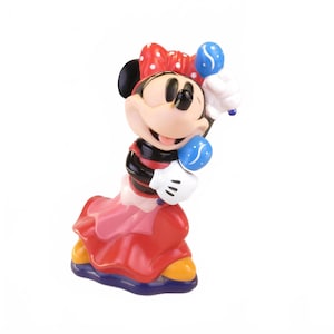 May include: A Minnie Mouse figurine, featuring a red dress, a red and white polka dot bow, and white gloves holding blue balloons. The figure has a smiling expression and is posed in a dynamic stance. The figurine is a collectible item.