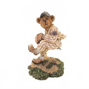 May include: A brown bear figurine in a baseball uniform, complete with a cap, glove, and striped jersey. The bear is posed mid-play on a grassy base, capturing a dynamic sports moment. The figurine is detailed with realistic textures and colors.