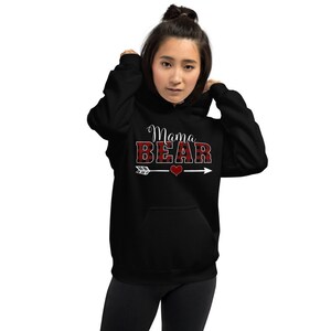 May include: Black hooded sweatshirt with the text "Mama Bear" in white lettering with a red and black buffalo plaid pattern. A white arrow with a red heart is below the text.