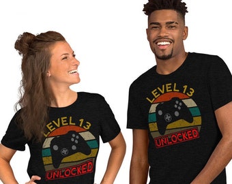May include: Two black t-shirts with a retro sunset graphic, a video game controller, and the text "Level 13 Unlocked".